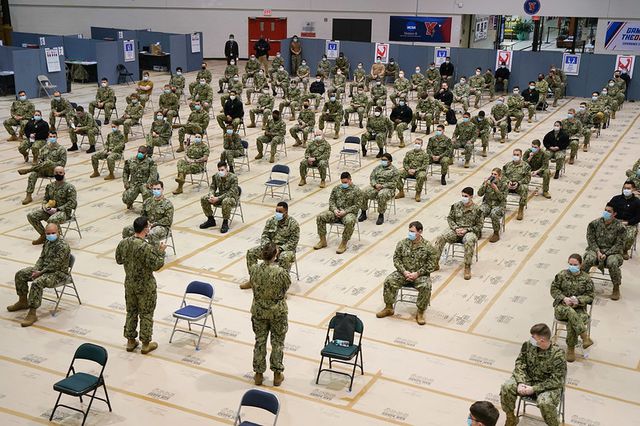 Rows of soldiers in fatigues sit on chairs inside a gym at York College during the announcement to open a mass FEMA-run state vaccination site there.